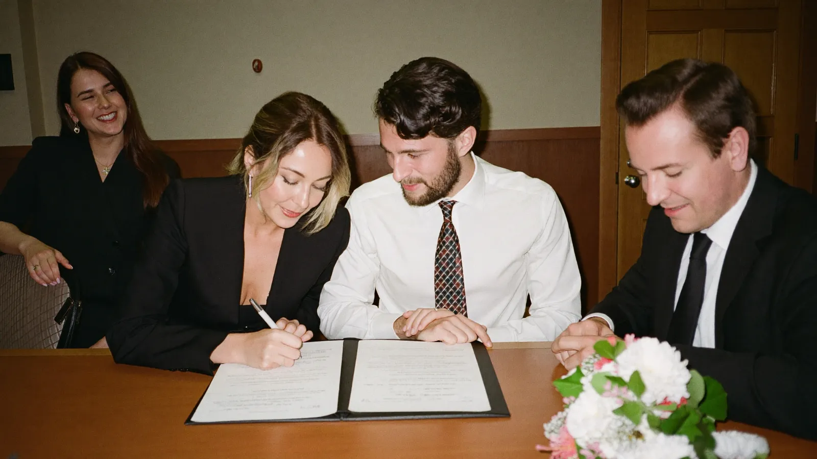 Couple signing the marriage register in front of a registrar with two witnesses beside them