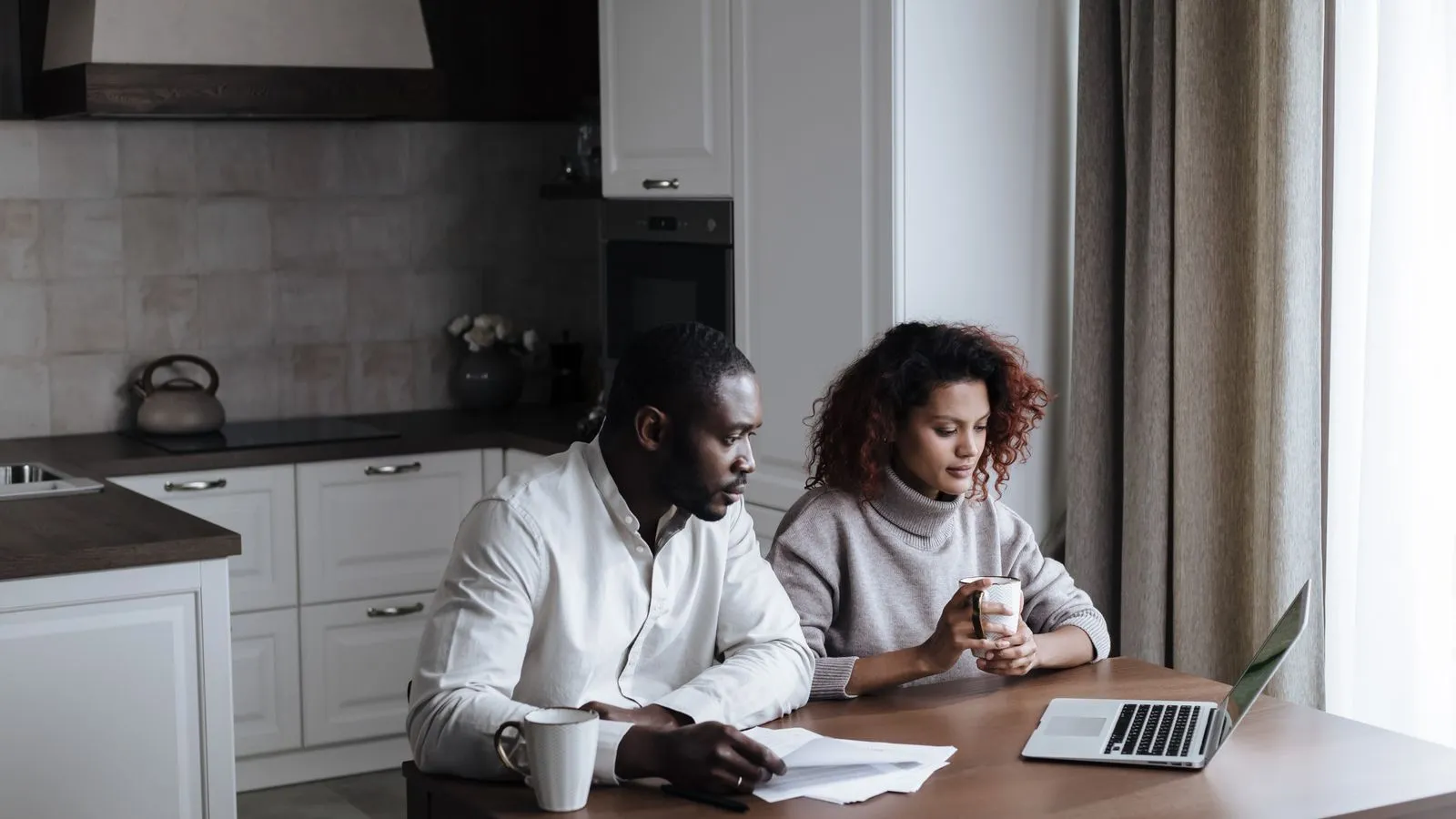 Young couple planning at a kitchen table with a laptop and papers