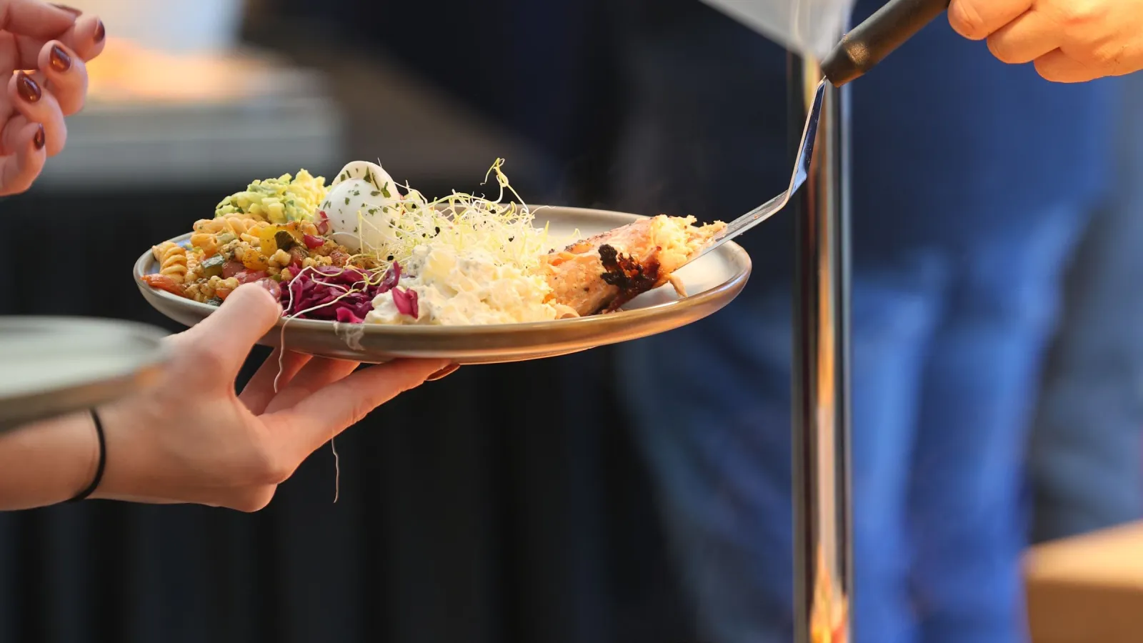 A server adding a hot dish to a guest's plate at a catered buffet