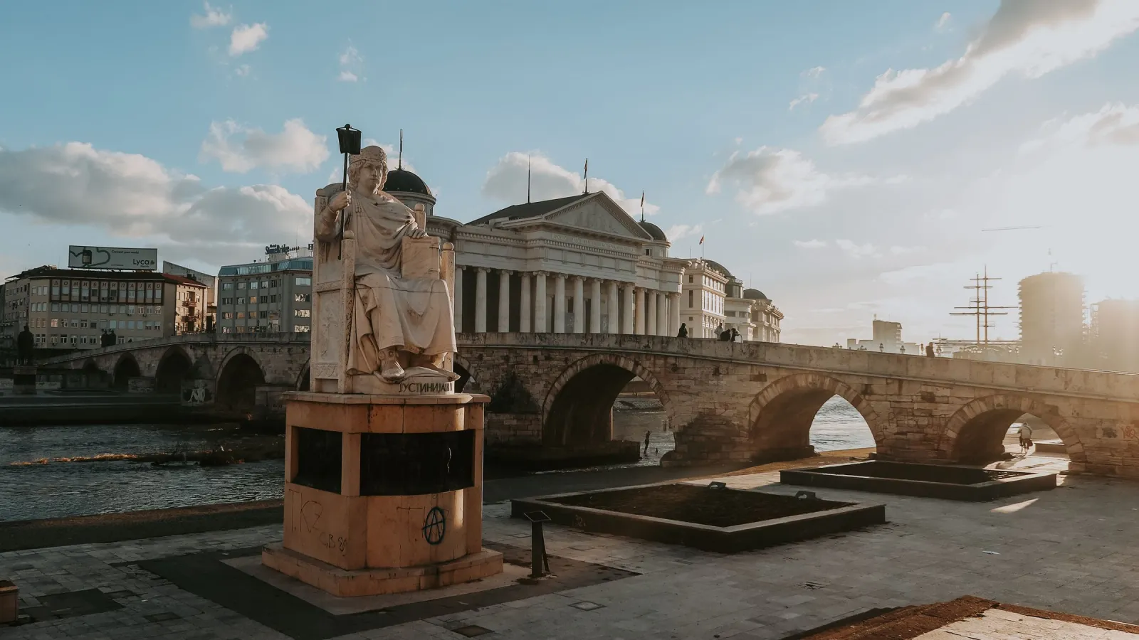 Ura e Gurit mbi Vardar në Shkup në perëndim të diellit, me një monument në breg dhe Muzeun Arkeologjik në sfond